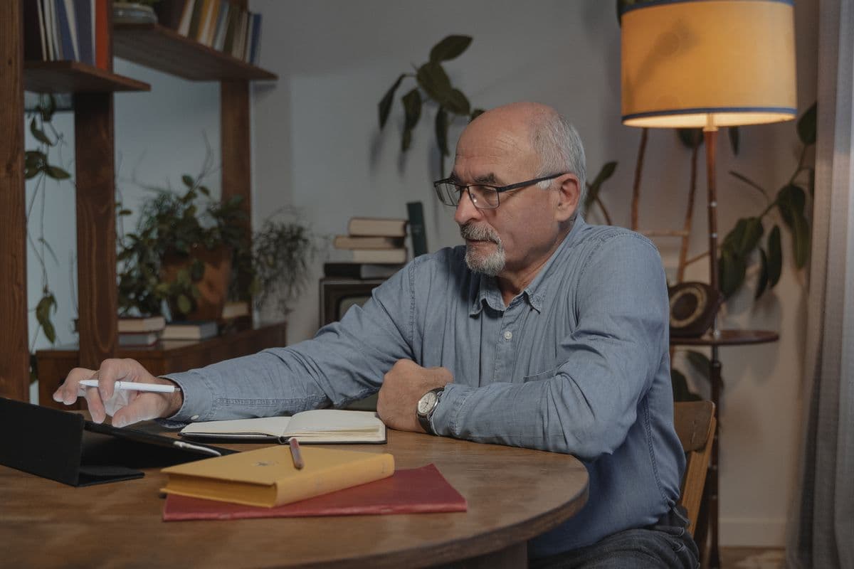 An older adult at a kitchen table reviewing notes before a medical appointment — organized, unhurried, dignified.